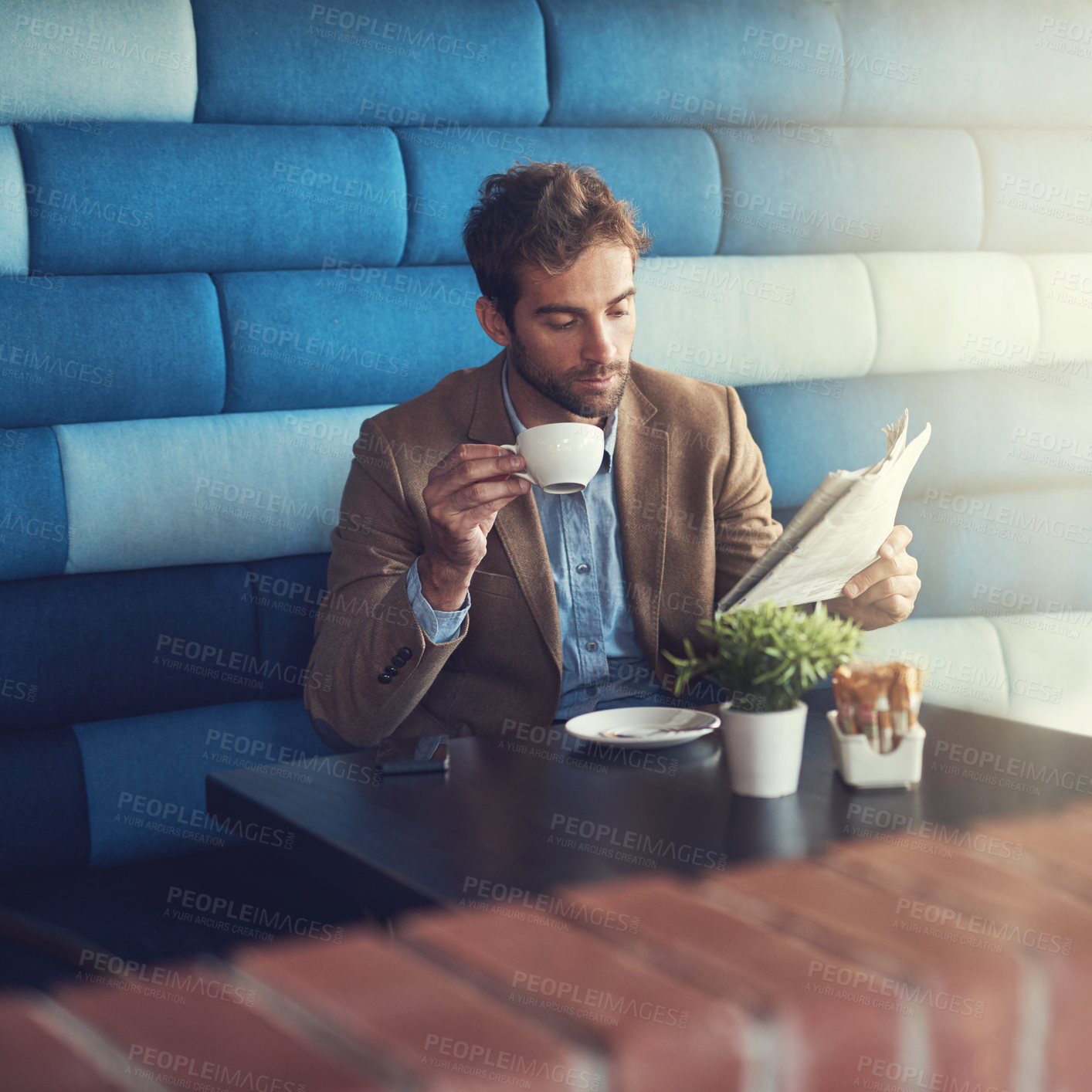 Buy stock photo Shot of a handsome man reading a newspaper on a coffee break in a cafe