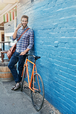 Buy stock photo Man, portrait and phone call outdoor by bicycle with communication, conversation and talking by brick wall. Person, face and happy with smartphone in city with bike for travel and commute on mockup