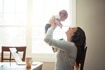 Buy stock photo Shot of a mother holding her newborn baby while sitting at a table in front of a laptop