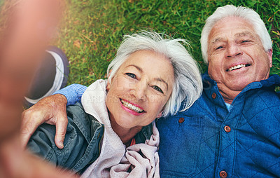 Buy stock photo Shot of a senior couple lying down on the grass and taking a selfie