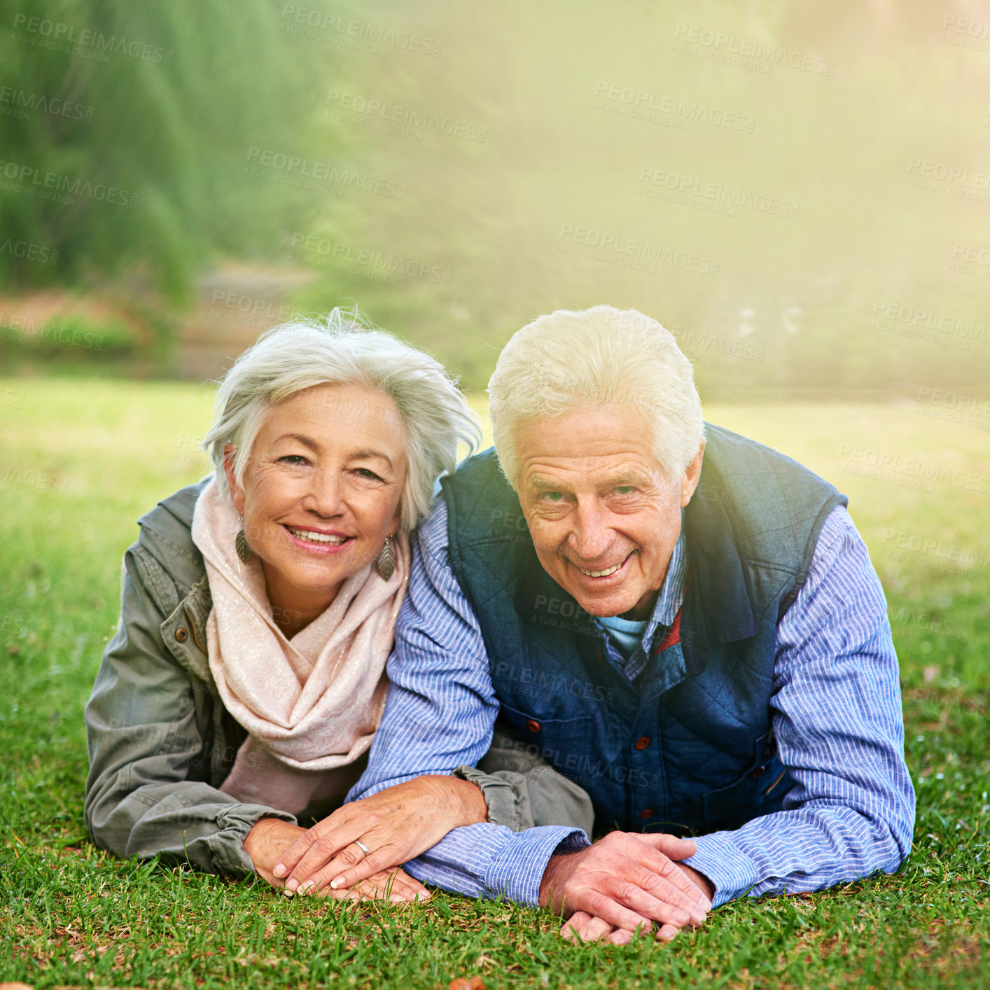 Buy stock photo Portrait of a happy senior couple lying down on the grass together in the park