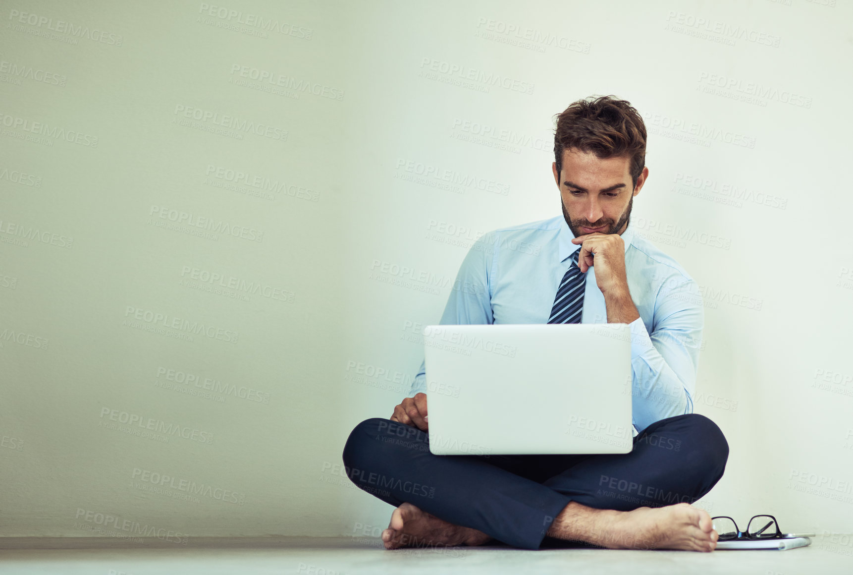 Buy stock photo Shot of a young corporate businessman sitting on the ground with a laptop