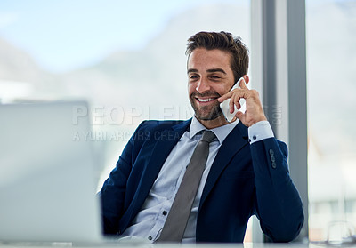 Buy stock photo Shot of a young corporate businessman sitting at a desk in front of a laptop and talking on a cellphone