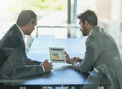 Buy stock photo Shot of two colleagues looking at a graph on a digital tablet together in an office