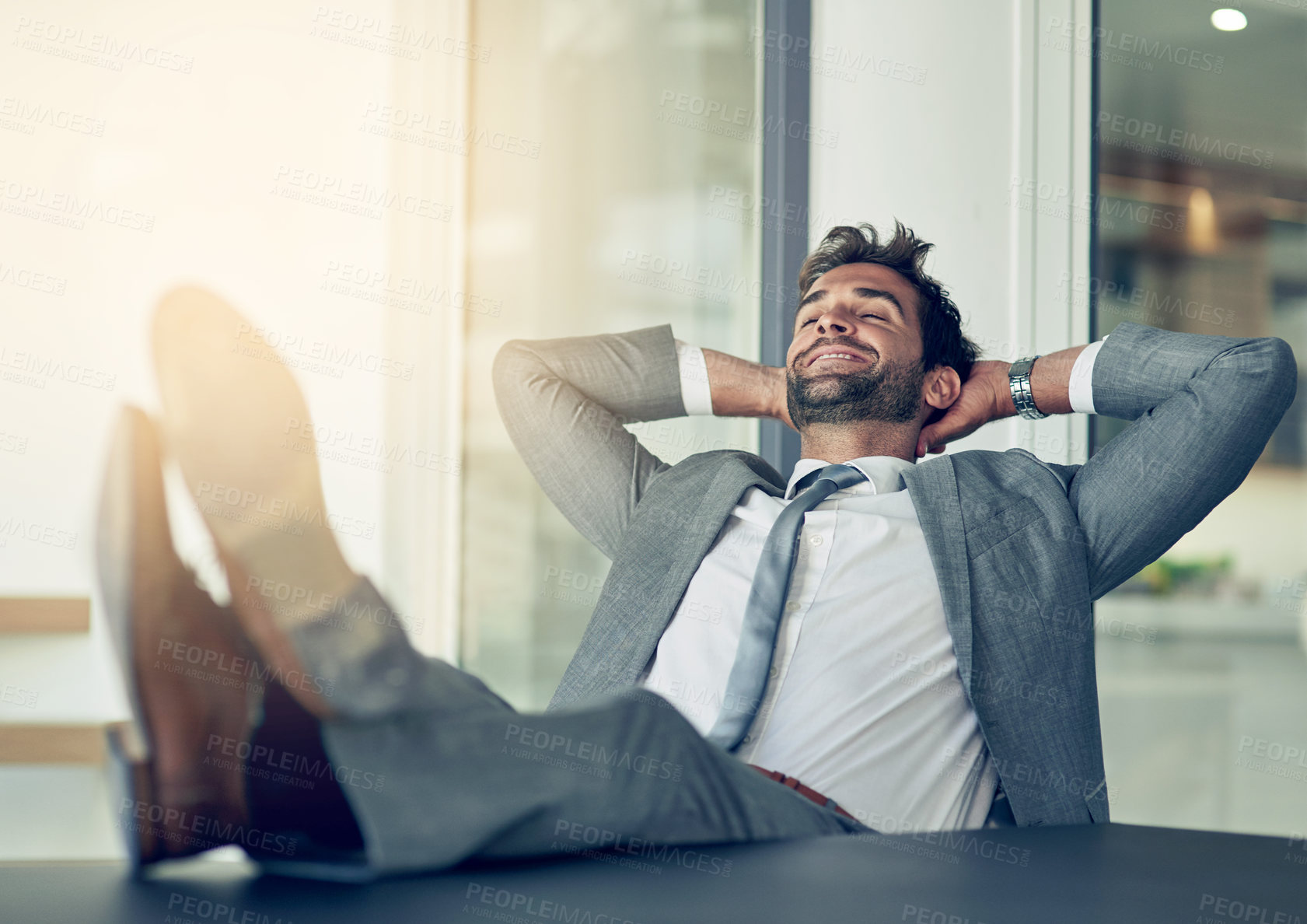Buy stock photo Shot of a businessman leaning back in his chair with his feet on a desk and hands behind his head