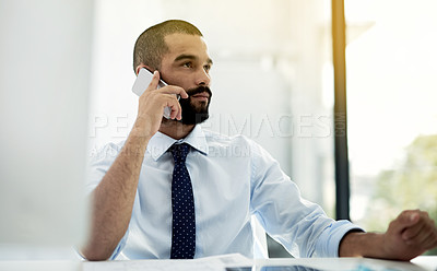 Buy stock photo Shot of a young businessman talking on the phone while working at his desk in an office