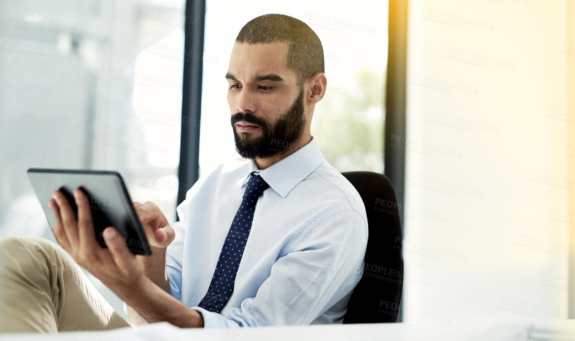 Buy stock photo Shot of a young businessman using a digital tablet at his desk in an office