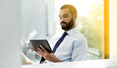 Buy stock photo Shot of a young businessman using a digital tablet at his desk in an office