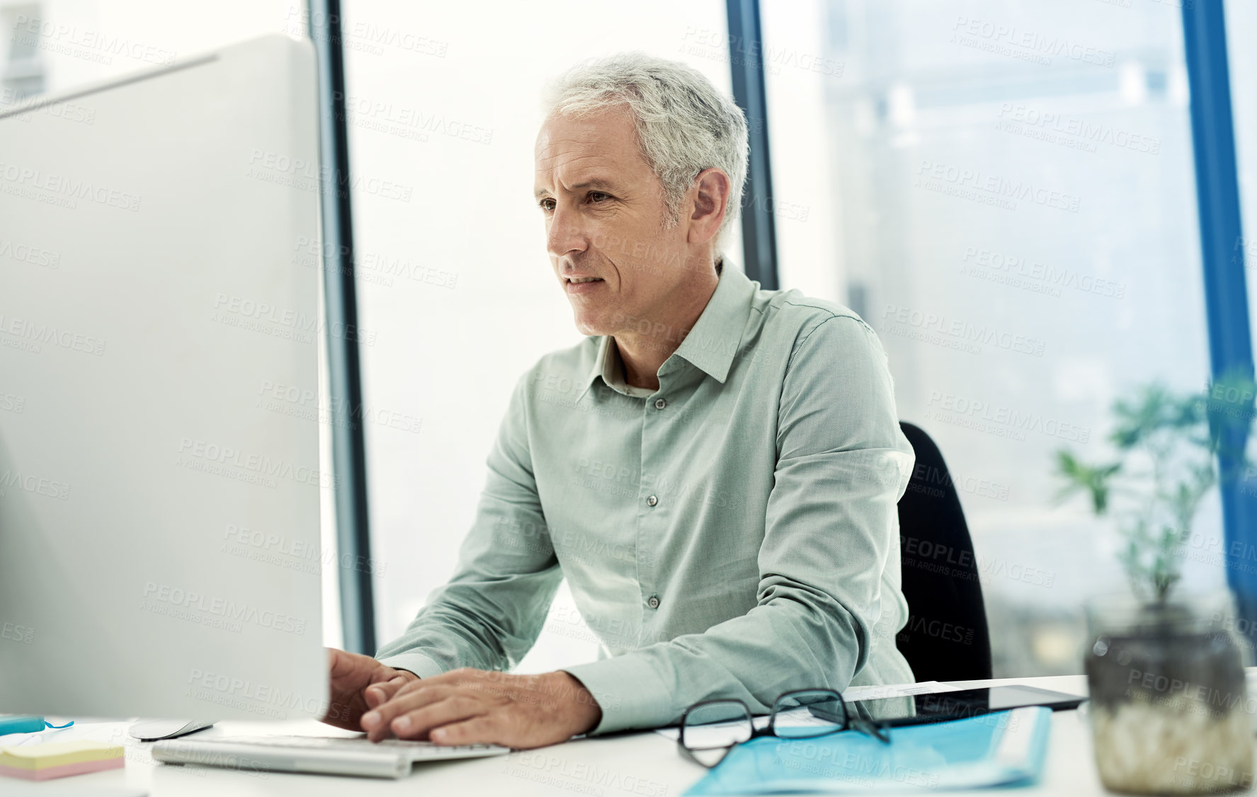 Buy stock photo Shot of a mature businessman working on a computer at his desk in an office