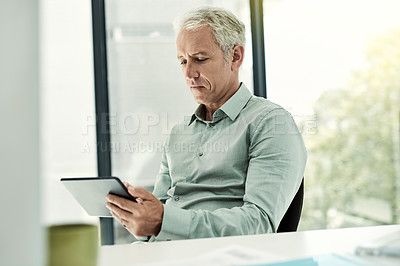 Buy stock photo Shot of a mature businessman using a digital tablet at his desk in an office