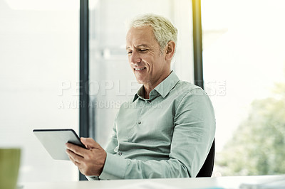Buy stock photo Shot of a mature businessman using a digital tablet at his desk in an office