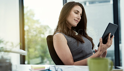 Buy stock photo Shot of a young businesswoman working on a digital tablet at her desk in an office
