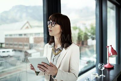 Buy stock photo Shot of a young businesswoman using a digital tablet while standing near a window in an office