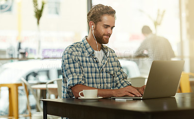 Buy stock photo Shot of a young man with earphones using a laptop in a cafe