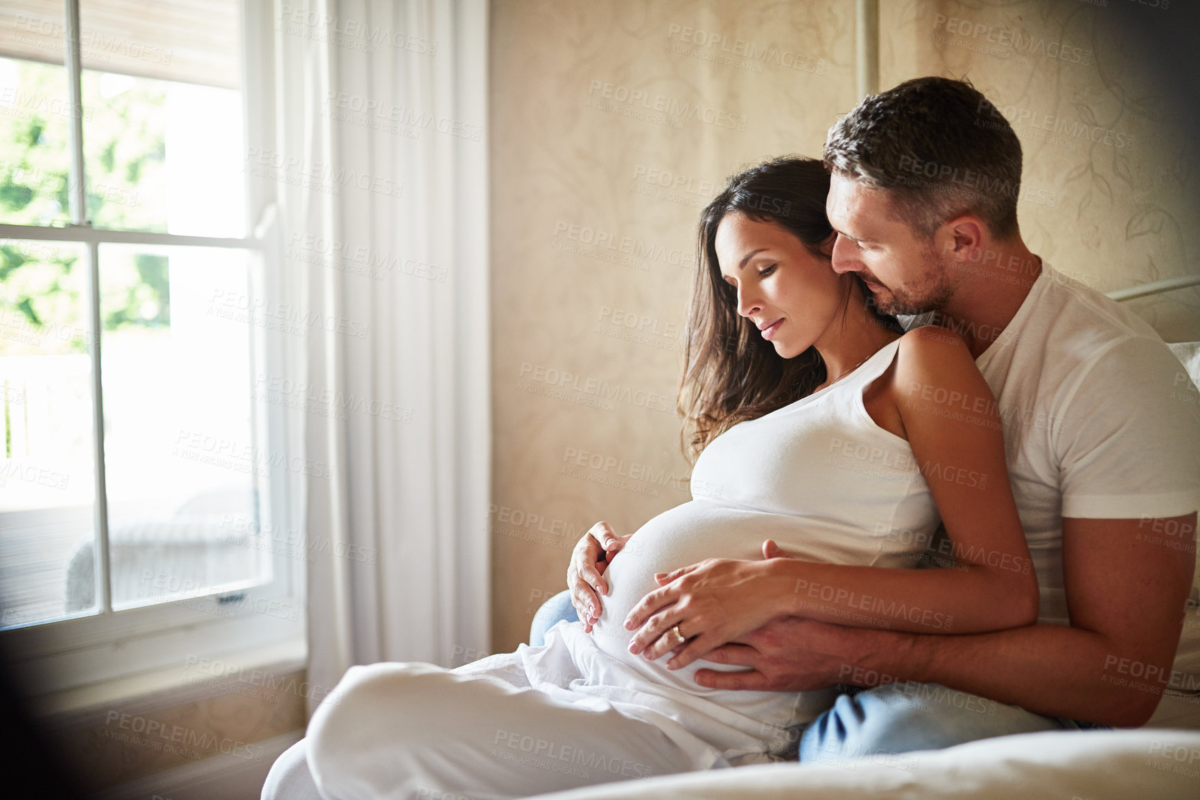 Buy stock photo Shot of a husband and pregnant wife sitting together in a bedroom