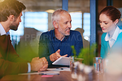 Buy stock photo Shot of businesspeople using a digital tablet in a meeting
