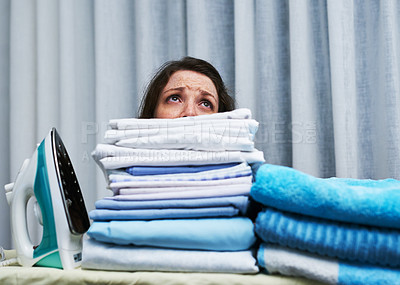 Buy stock photo Shot of an anxious looking young woman behind a pile of laundry on an ironing board