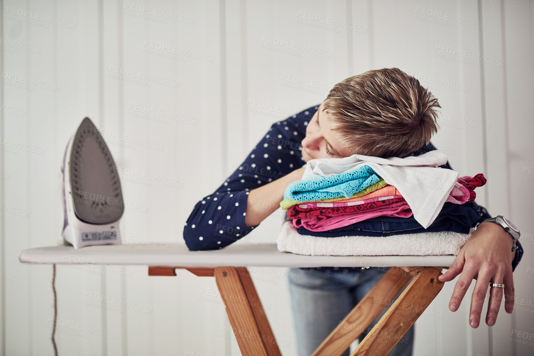 Buy stock photo Shot of a woman with her head down on a pile of clothes on an ironing board