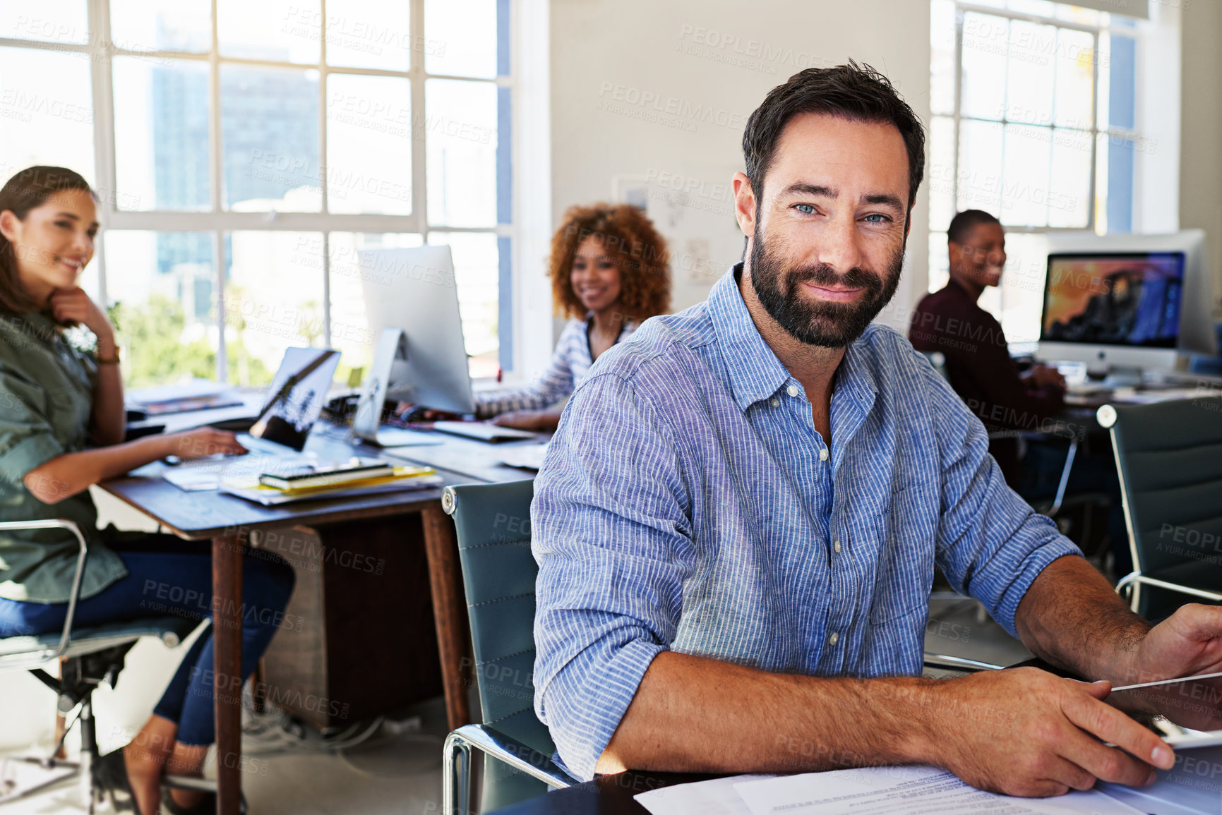 Buy stock photo Portrait of man in creative agency with leadership, confidence and success at design startup. Happy business people in modern office, manager or team leader working at desk with digital technology.