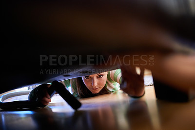 Buy stock photo Shot of a young woman vacuuming underneath a piece of furniture