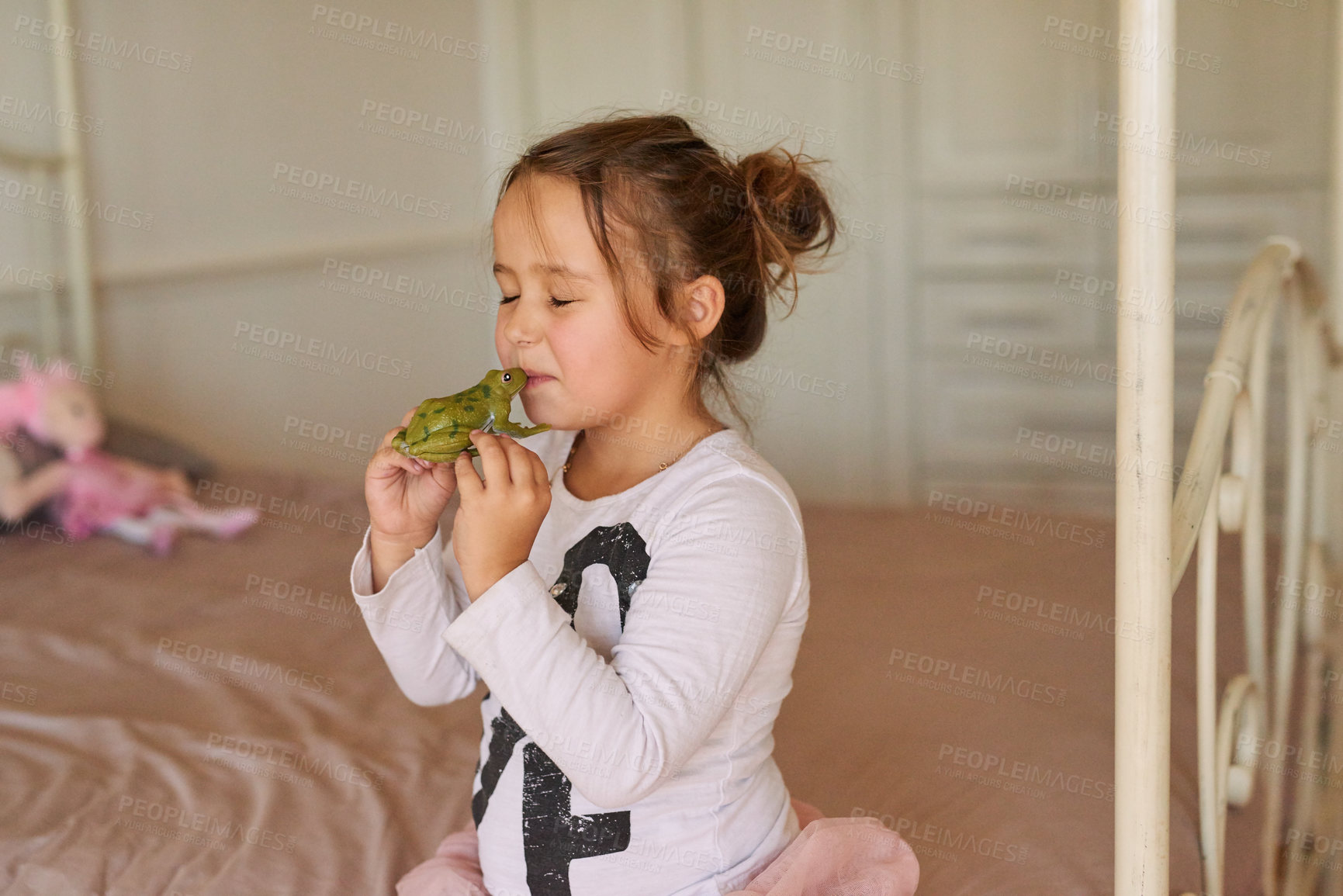 Buy stock photo Child, toy and girl kissing frog in bedroom for fairytale, happiness or playing in family home. Kiss, pretend and young kid on bed with object in playroom for having fun, playful or game in apartment