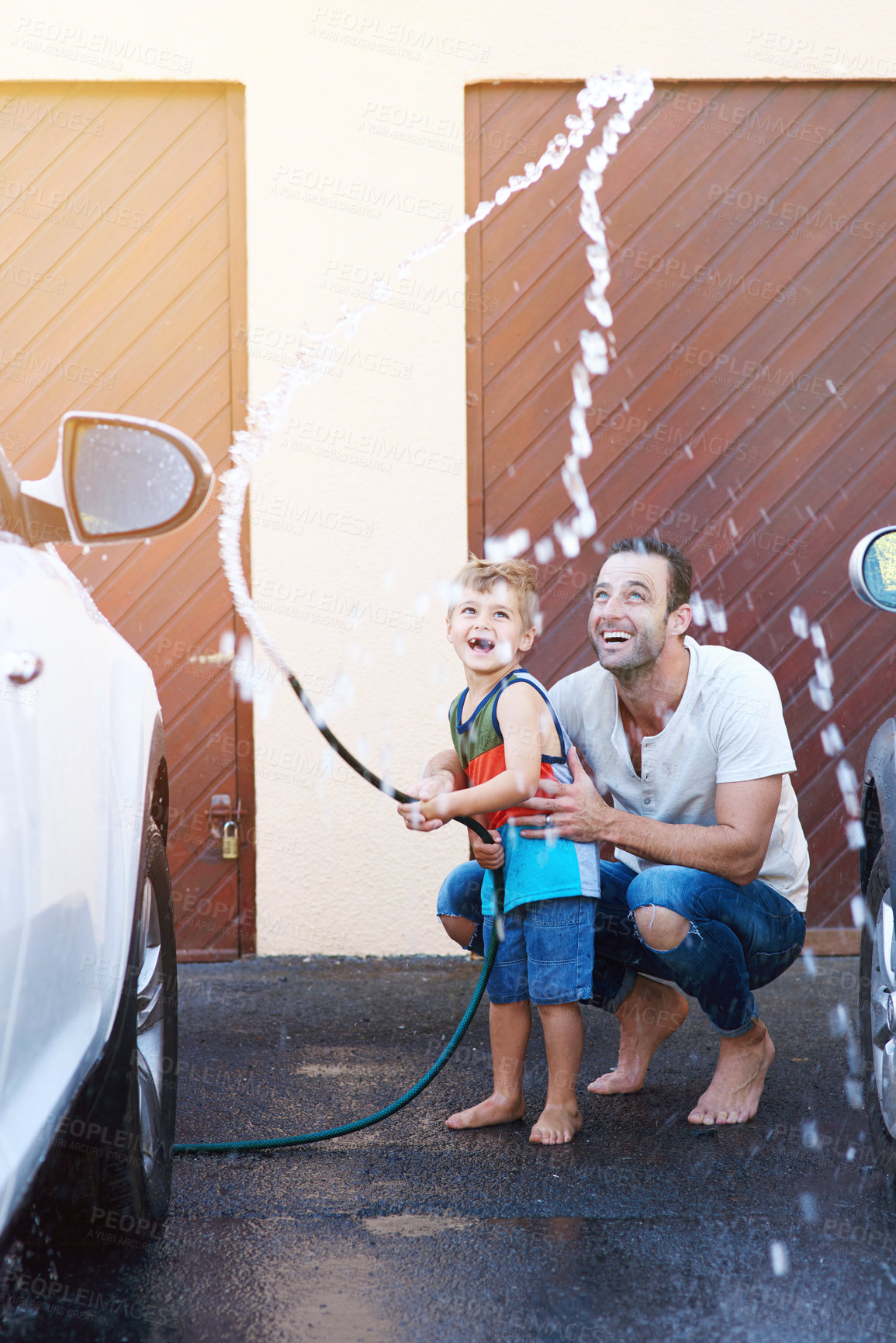 Buy stock photo Full length shot of a father and son playing with a hosepipe while washing a car together