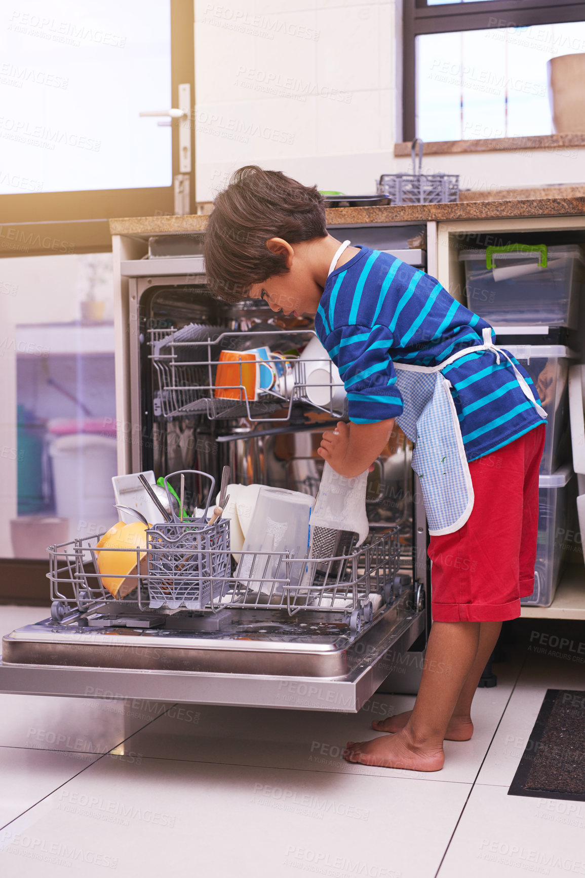 Buy stock photo Shot of a young boy busy at a dishwashing machine