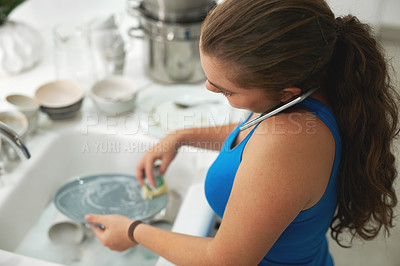 Buy stock photo Shot of a woman talking on a cellphone while washing dishes