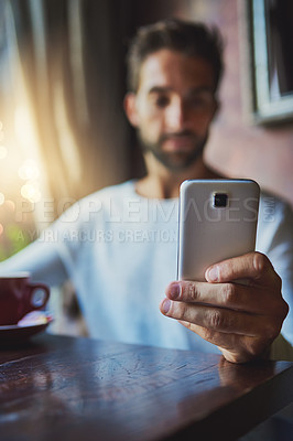 Buy stock photo Cropped shot of a young man using his cellphone in a coffee shop