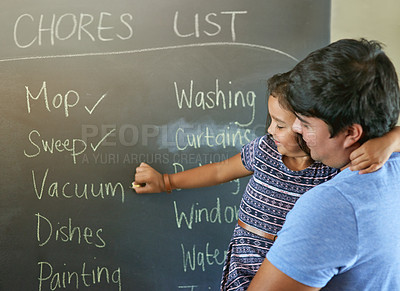 Buy stock photo Shot of a father holding his daughter while she marks off chores on a chalkboard