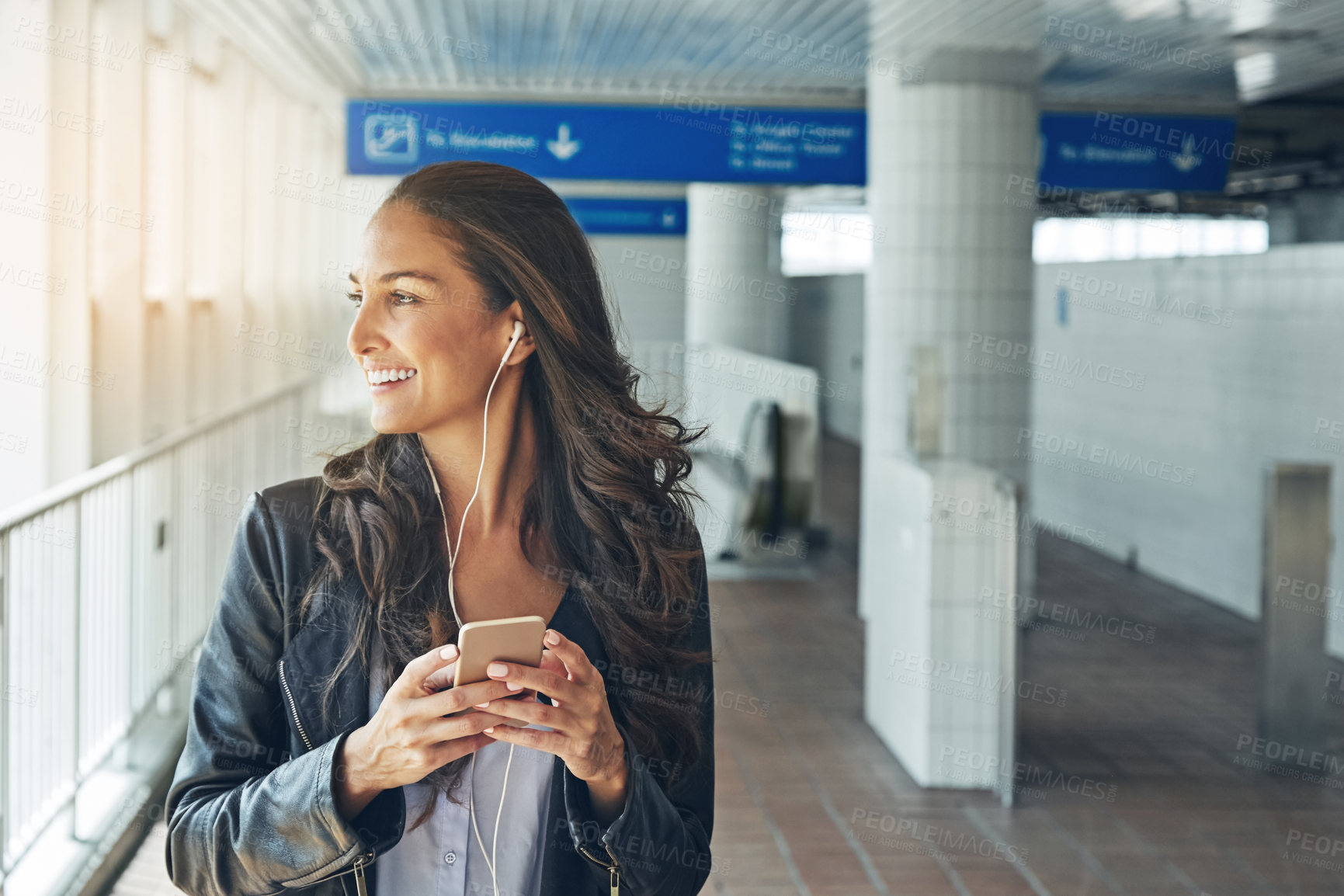 Buy stock photo Shot of a young woman listening to music on a phone in an urban setting