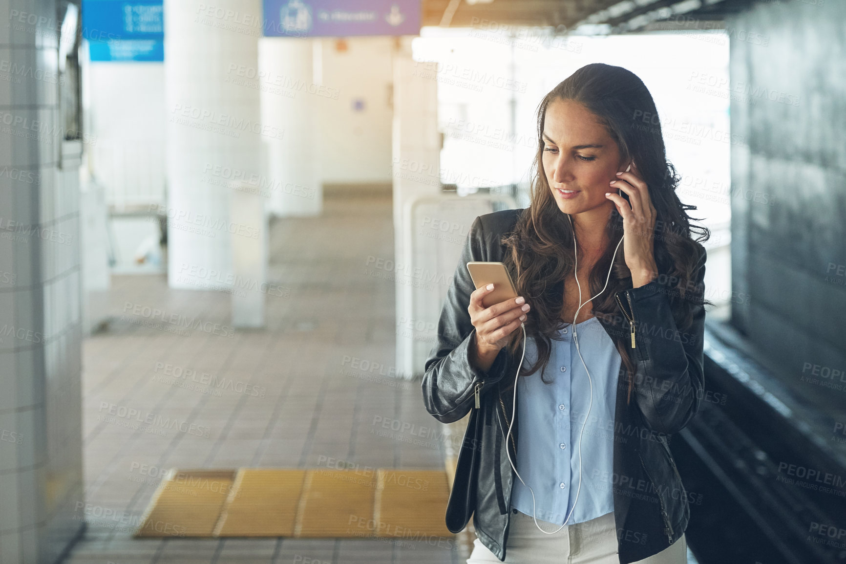 Buy stock photo Shot of a young woman listening to music on a phone in an urban setting