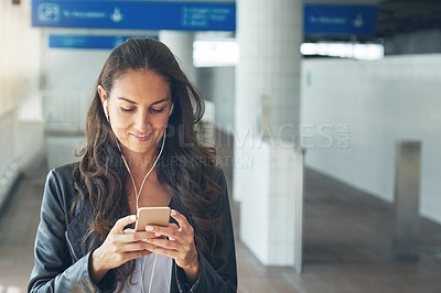 Buy stock photo Shot of a young woman listening to music on a phone in an urban setting