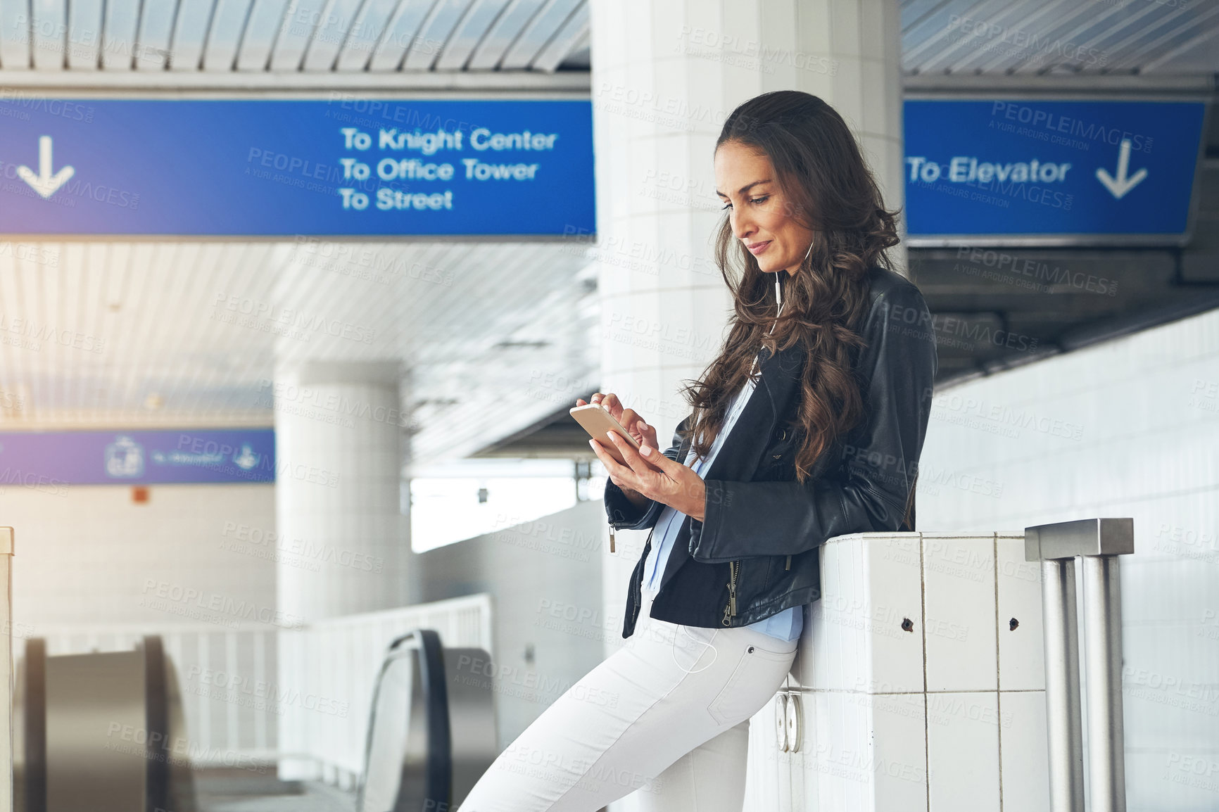 Buy stock photo Shot of a young woman listening to music on a phone in an urban setting