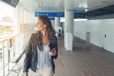 Buy stock photo Shot of a young woman listening to music on a phone in an urban setting