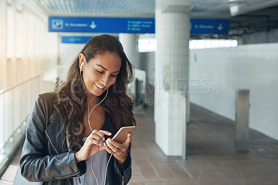 Buy stock photo Shot of a young woman listening to music on a phone in an urban setting