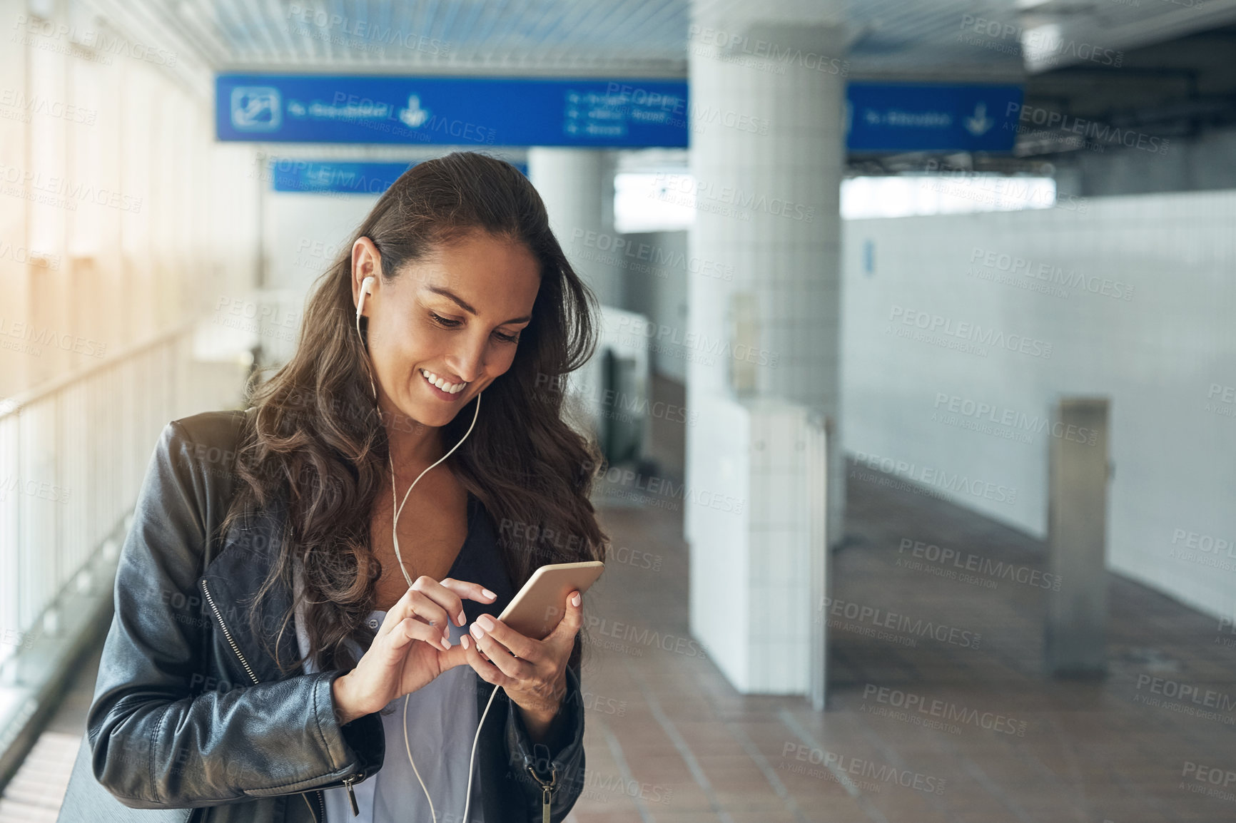 Buy stock photo Shot of a young woman listening to music on a phone in an urban setting