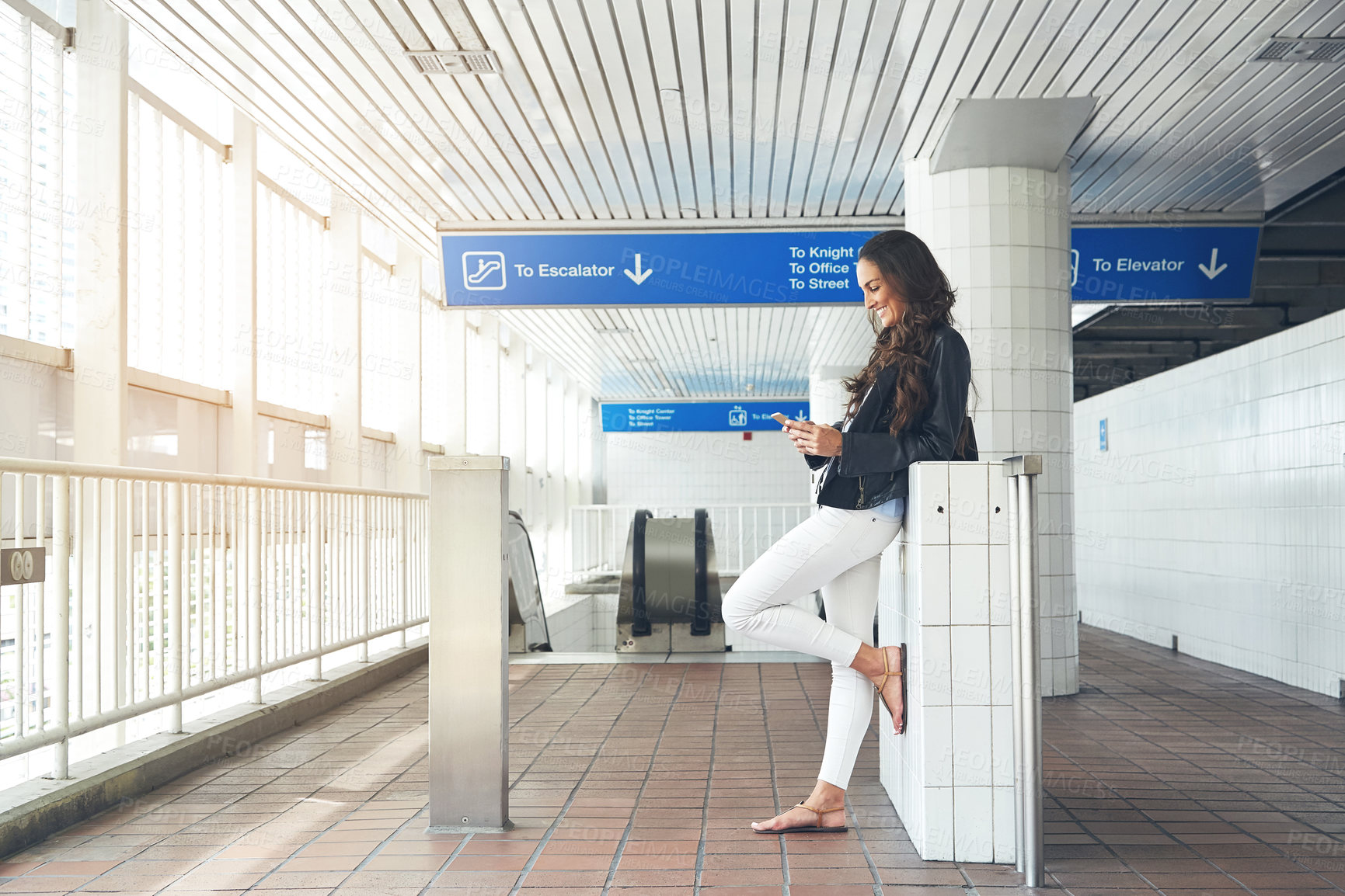 Buy stock photo Shot of a young woman listening to music on a phone in an urban setting