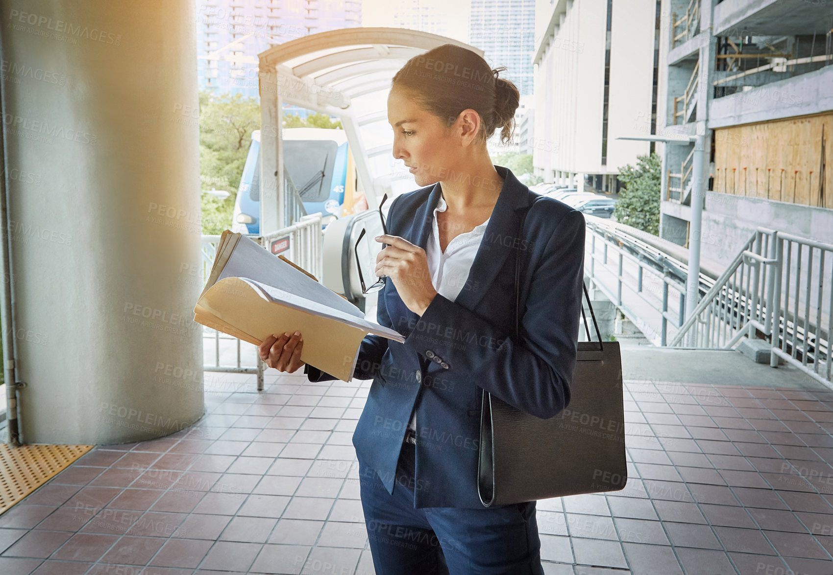 Buy stock photo Shot of a young businesswoman reading paperwork on her way to the office