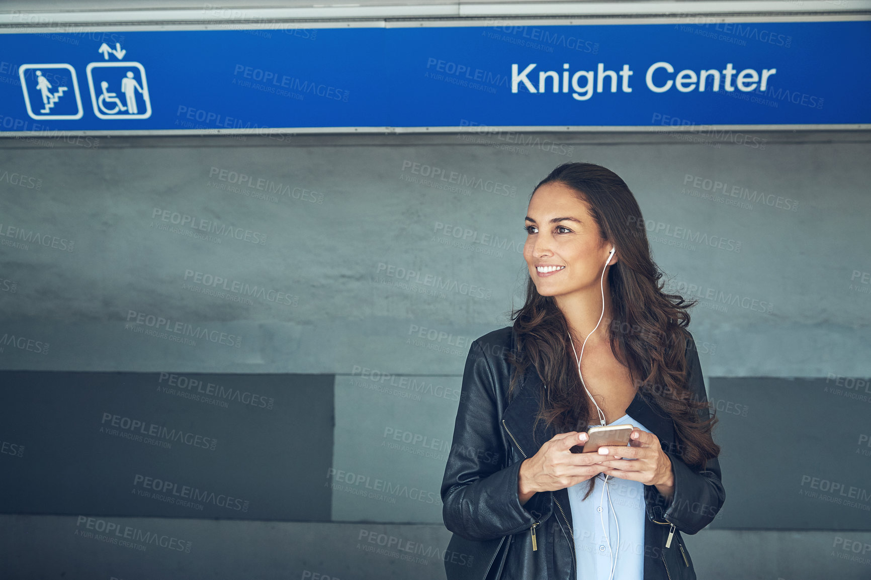 Buy stock photo Shot of a young woman listening to music on a phone in an urban setting