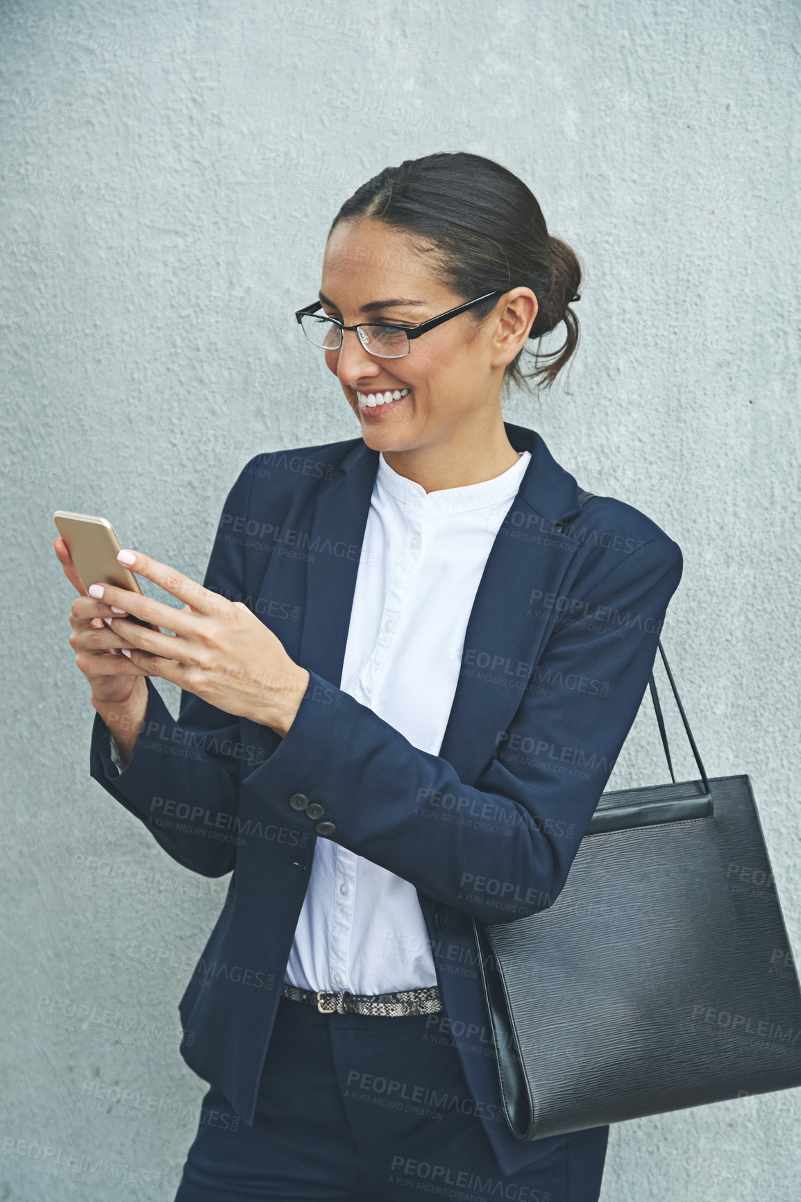 Buy stock photo Shot of a young businesswoman using her phone while standing against a gray wall