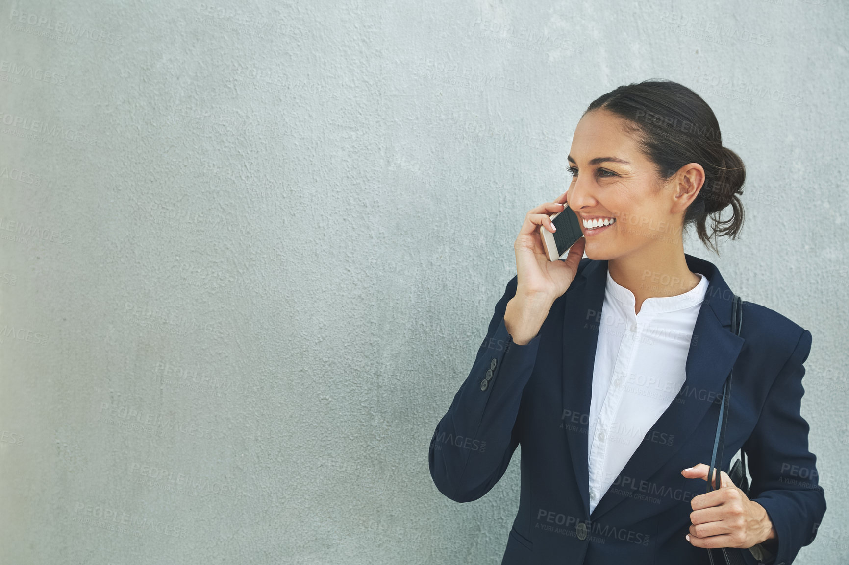 Buy stock photo Shot of a young businesswoman using her phone while standing against a gray wall