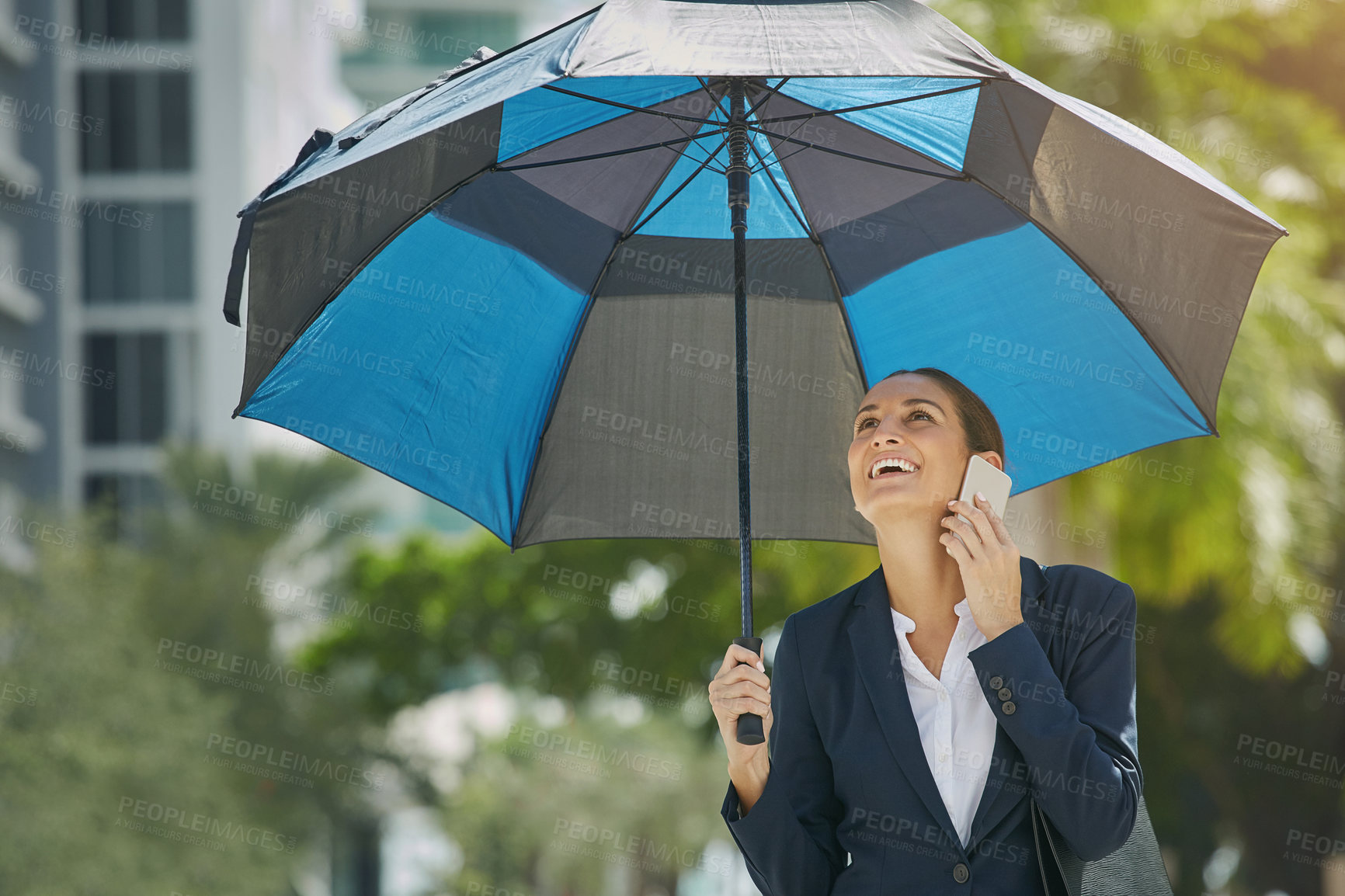 Buy stock photo Shot of a young businesswoman talking on her phone and holding an umbrella while out in the city