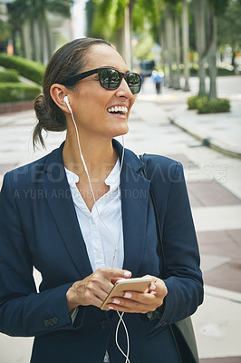 Buy stock photo Shot of a young businesswoman her phone and earphones while out in the city