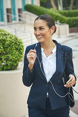 Buy stock photo Shot of a young businesswoman her phone and earphones while out in the city