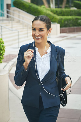 Buy stock photo Shot of a young businesswoman her phone and earphones while out in the city