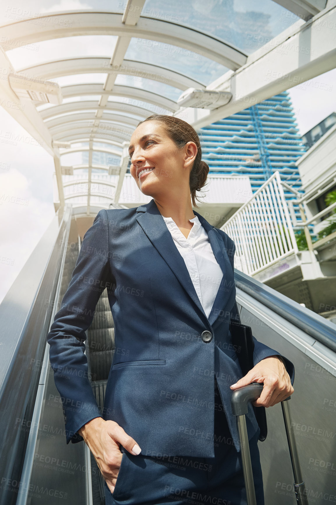 Buy stock photo Shot of a young businesswoman standing on an escalator on her way to work