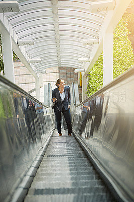 Buy stock photo Shot of a young businesswoman using a cellphone on an escalator