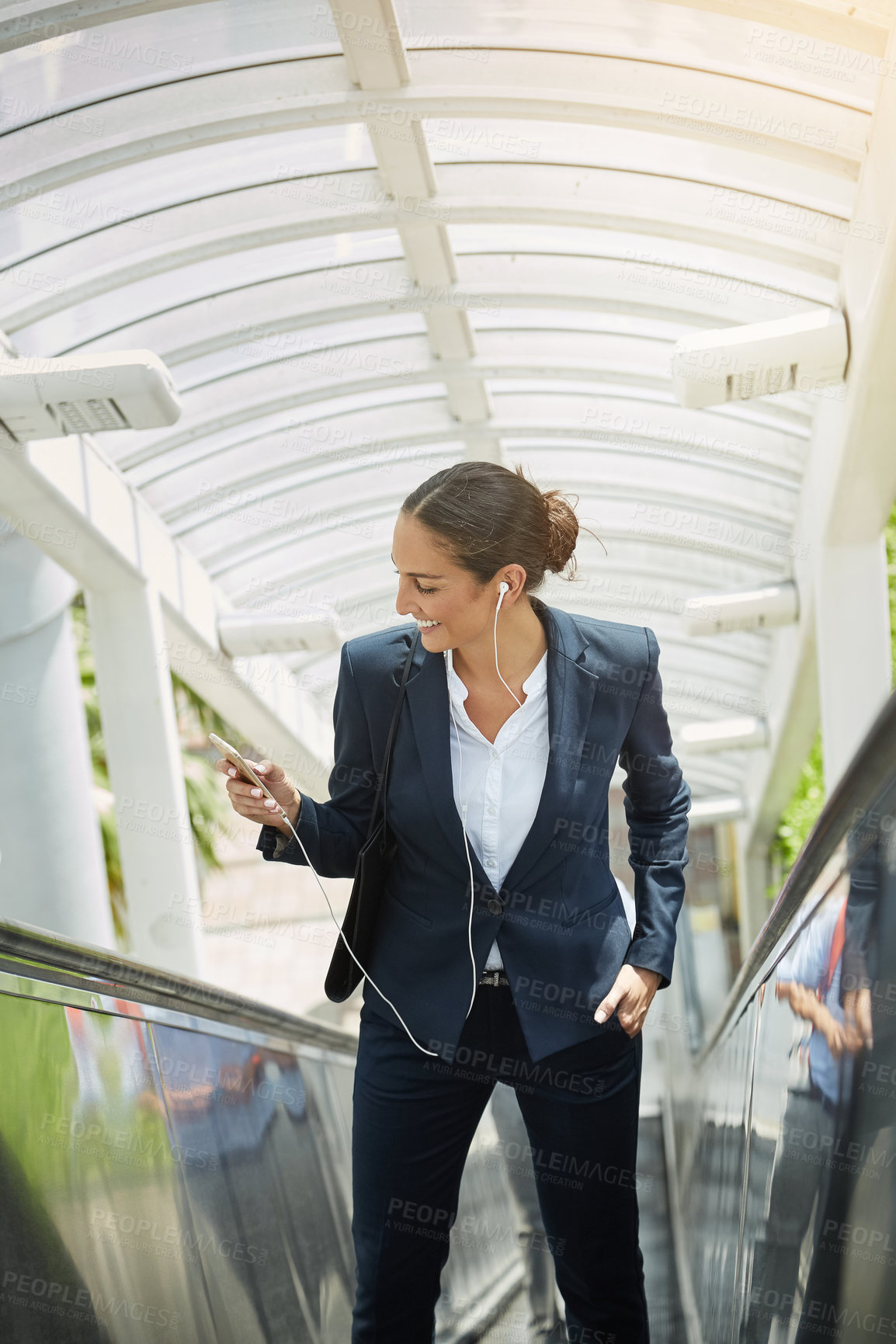 Buy stock photo Shot of a young businesswoman using a cellphone on an escalator