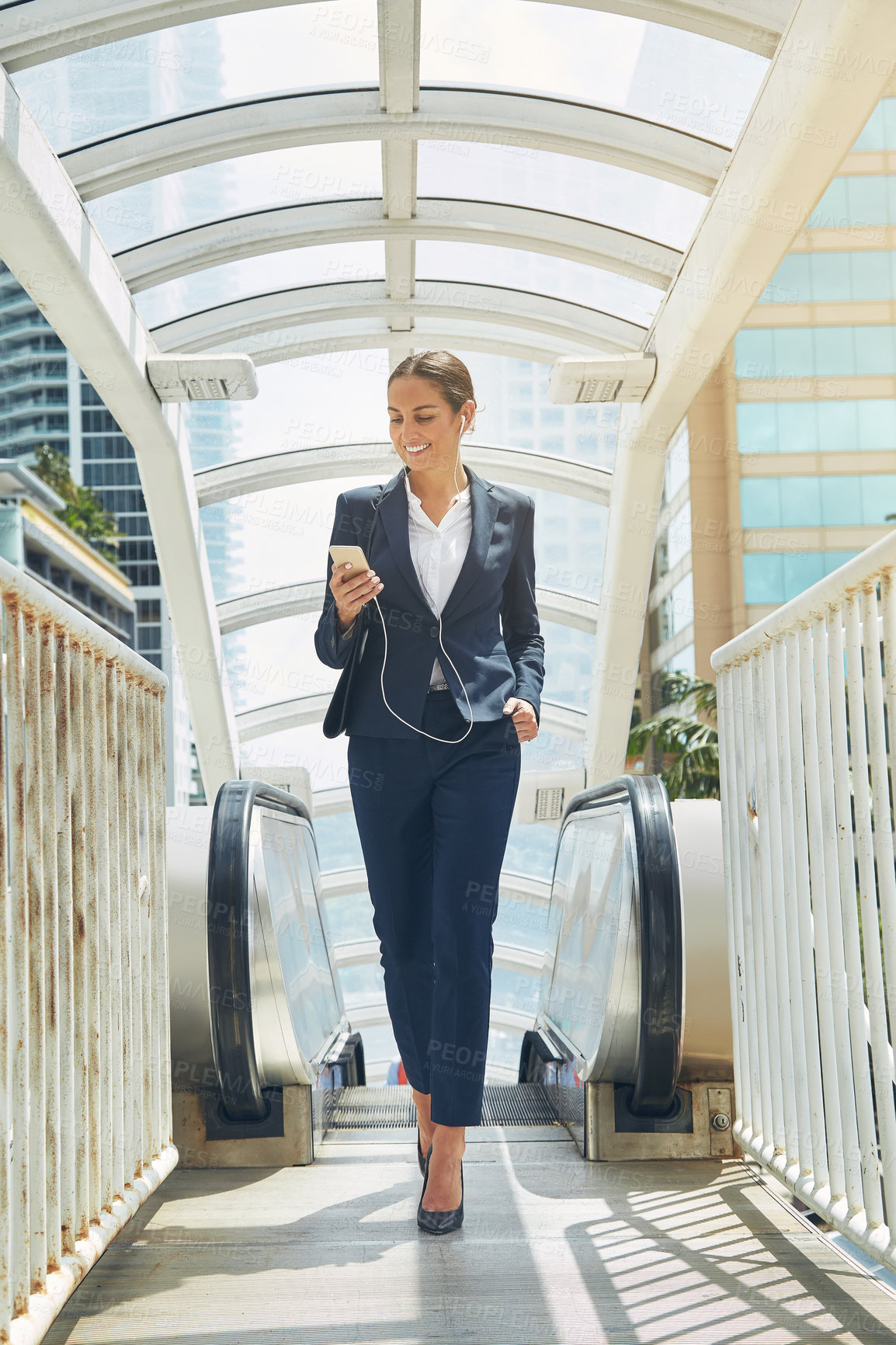 Buy stock photo Shot of a young businesswoman using a cellphone while getting off an escalator